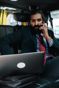Professional man in a taxi working on laptop and talking on phone.